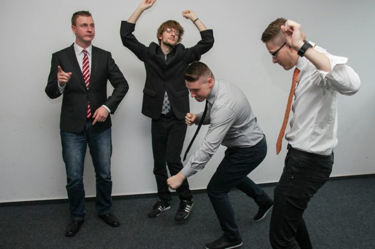 Vier Männer in Anzügen feiern ausgelassen in einem modernen Raum ihre Mitarbeiterzufriedenheit. 